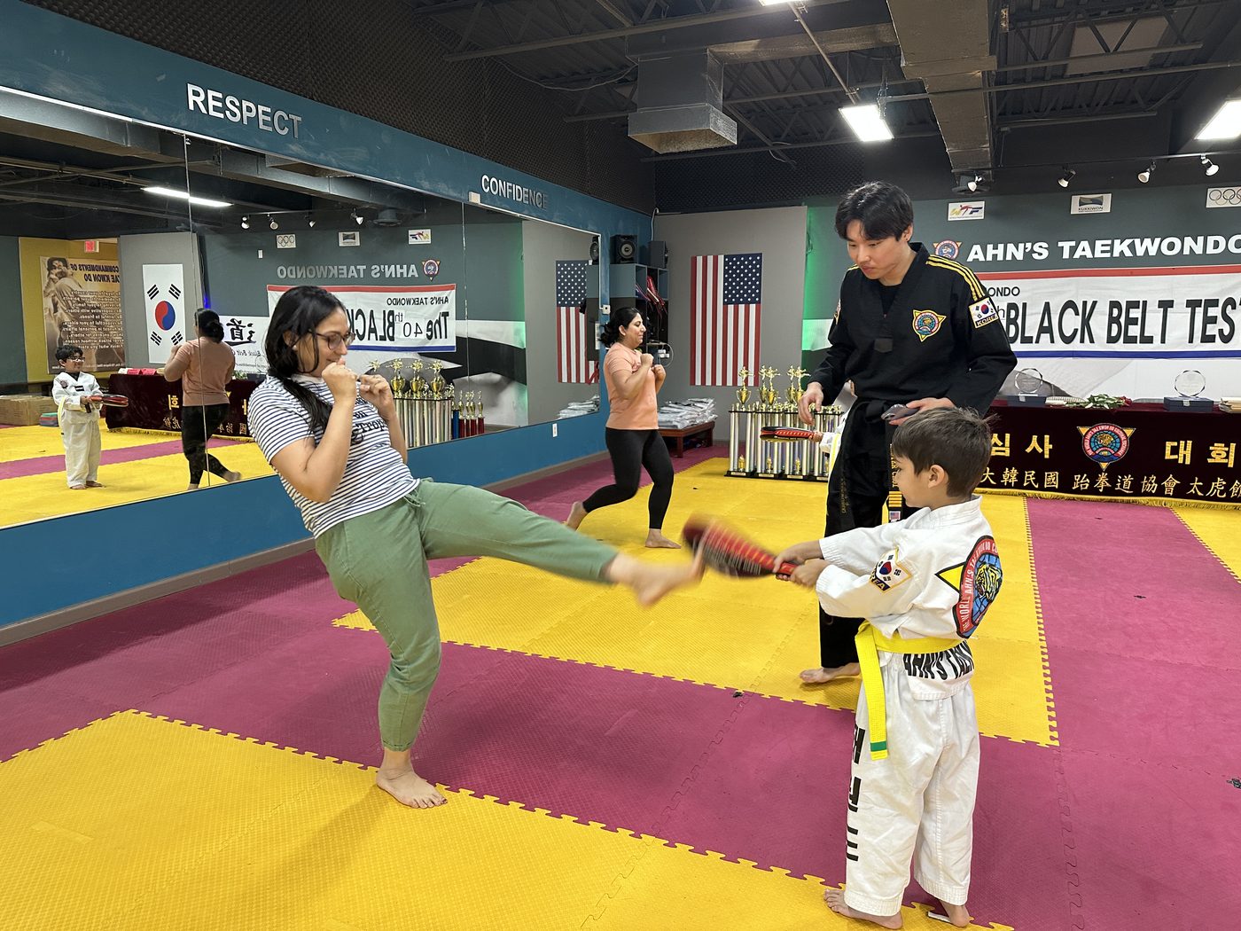 Parent practicing kicks with an instructor and child holding the pad