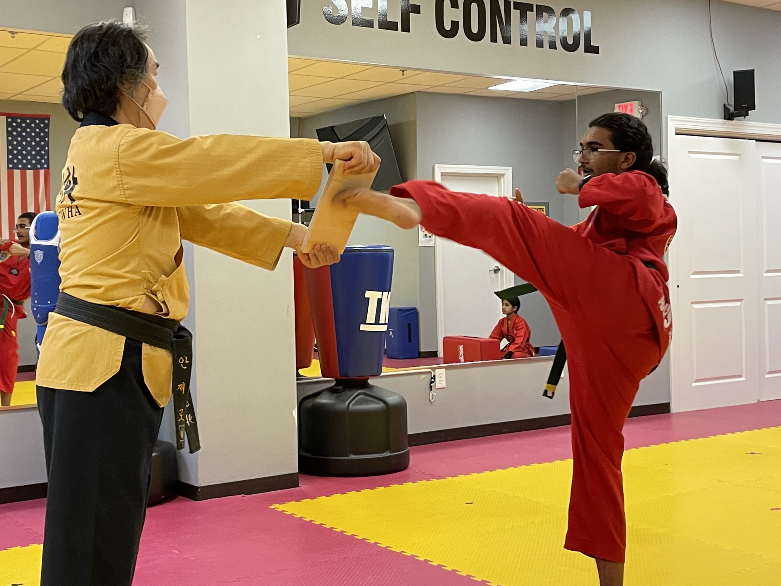 Master holding a kicking target for a student during class
