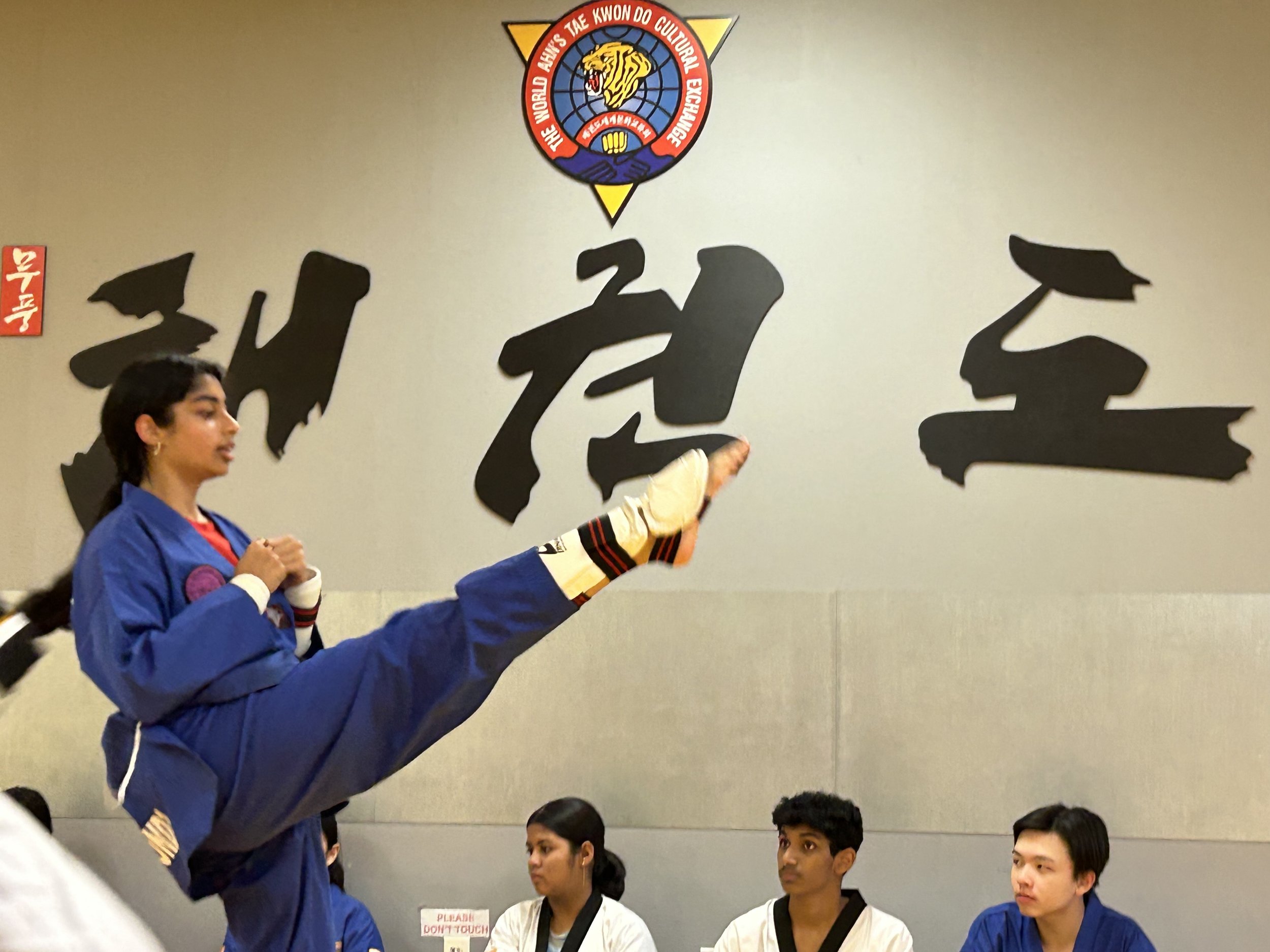 Student performing a side kick in front of the Taekwondo calligraphy wall at Ahn's Taekwondo