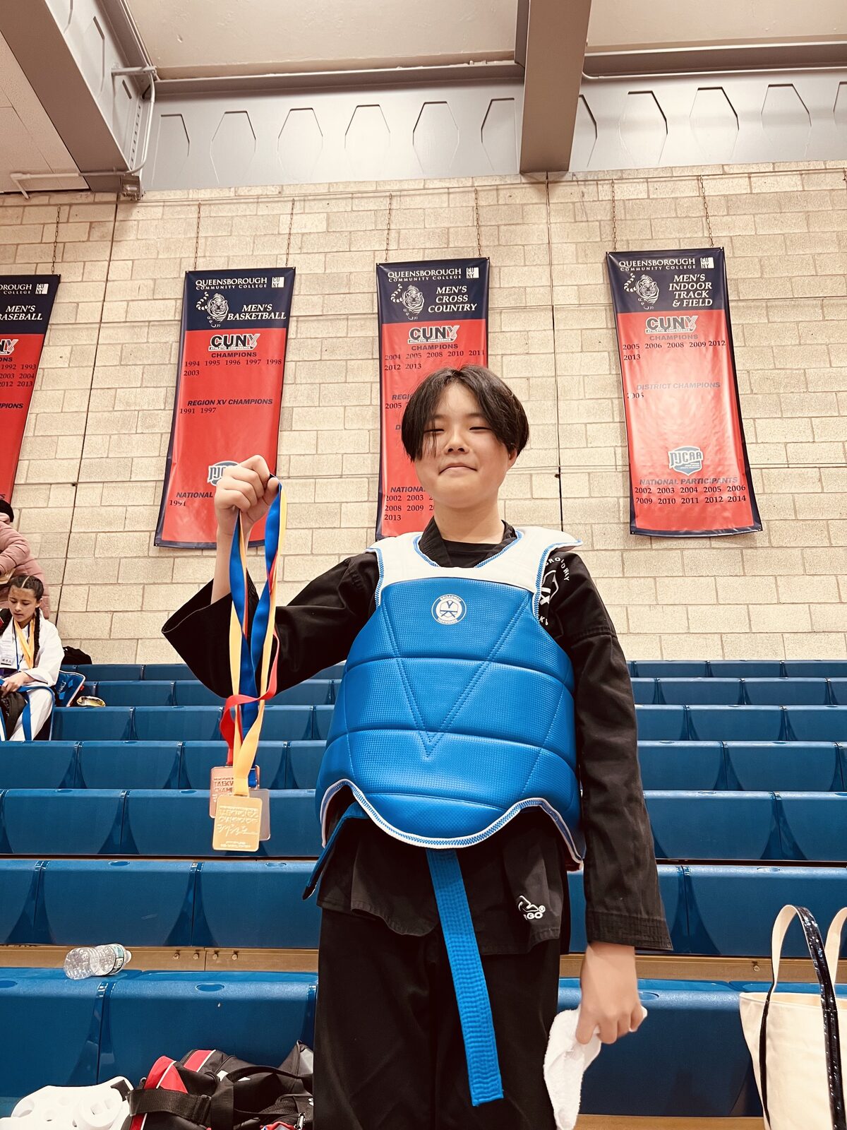 A young athlete in sparring gear holding up a medal